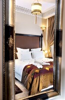 Camera d'hotel con un ampio specchio, un letto con lenzuola bianche, una testiera decorativa e un lampadario.