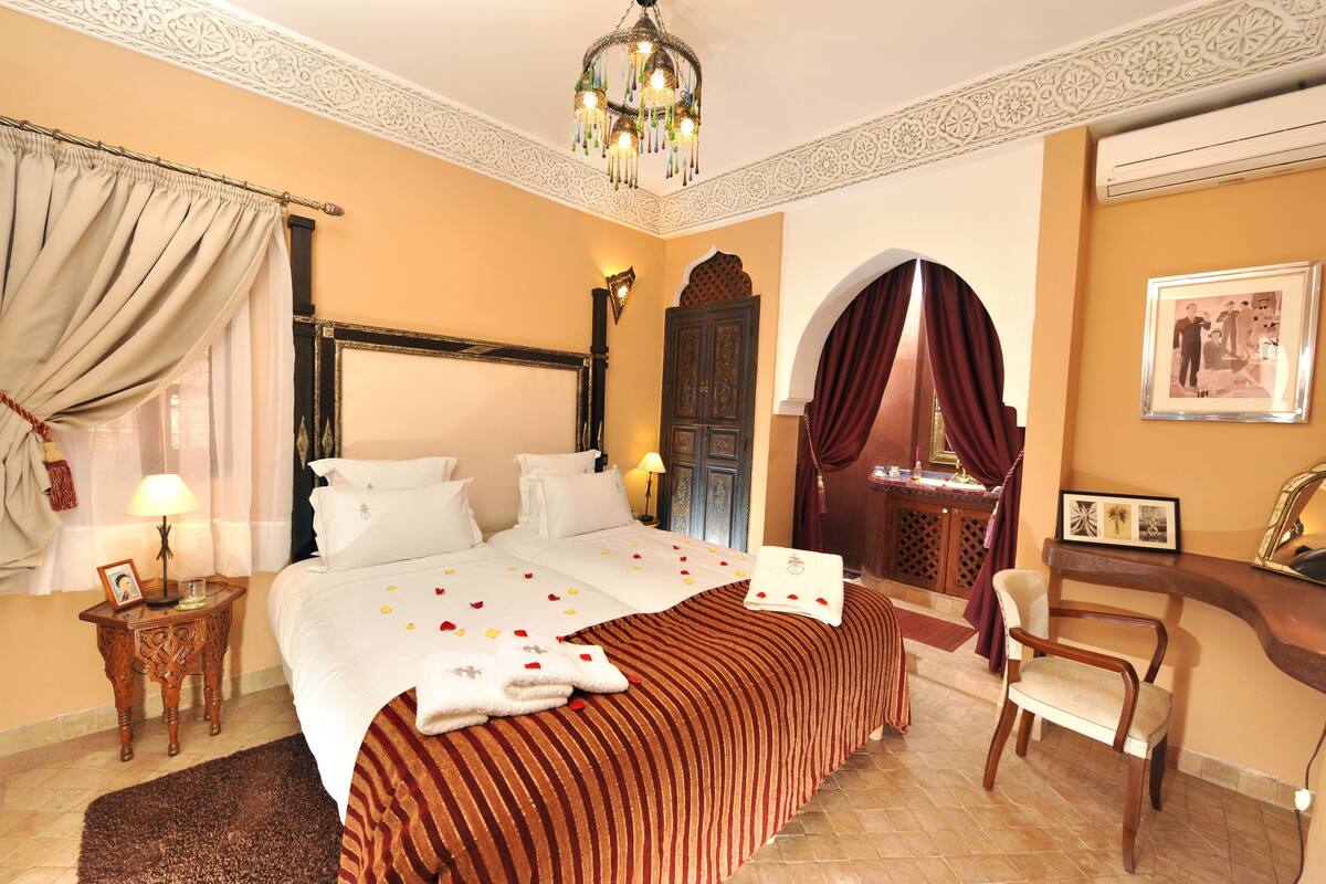Habitación de hotel con una cama grande, una zona de estar con una silla, un escritorio y un techo decorativo.