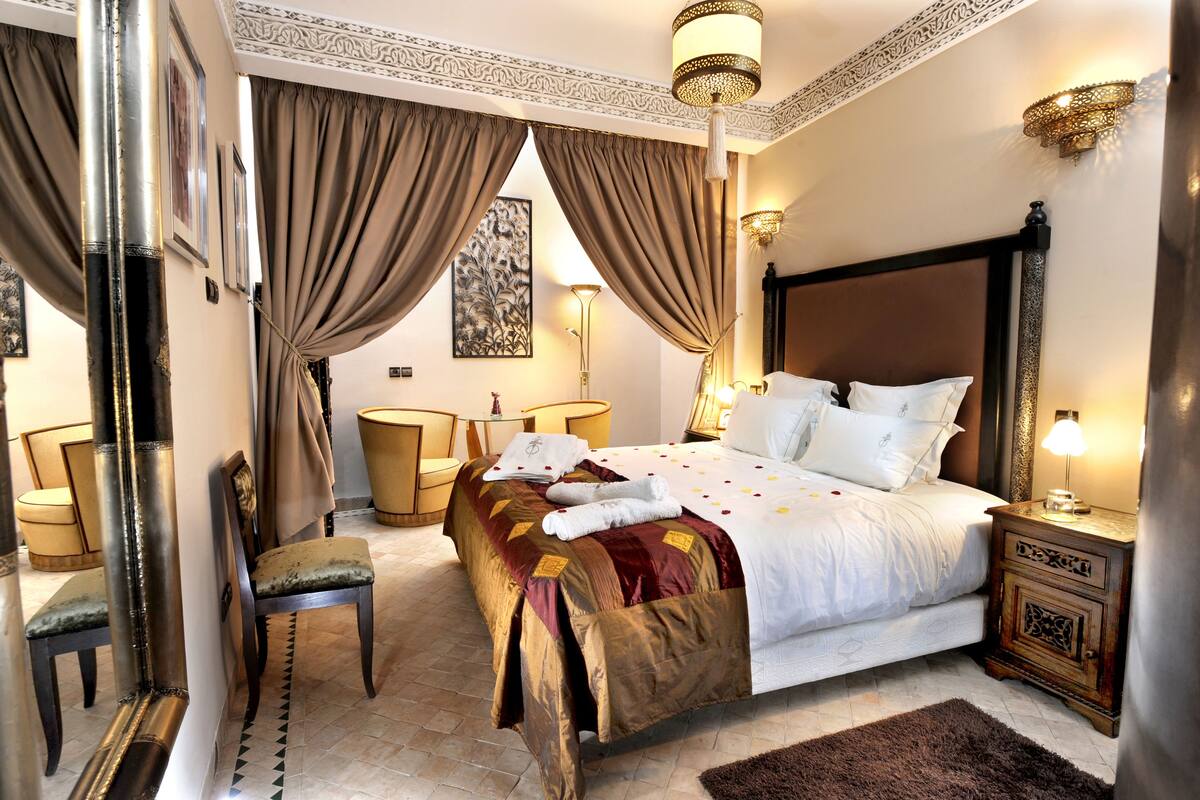 Un dormitorio elegante con una cama grande, una mesita de noche, una silla y una lámpara decorativa.