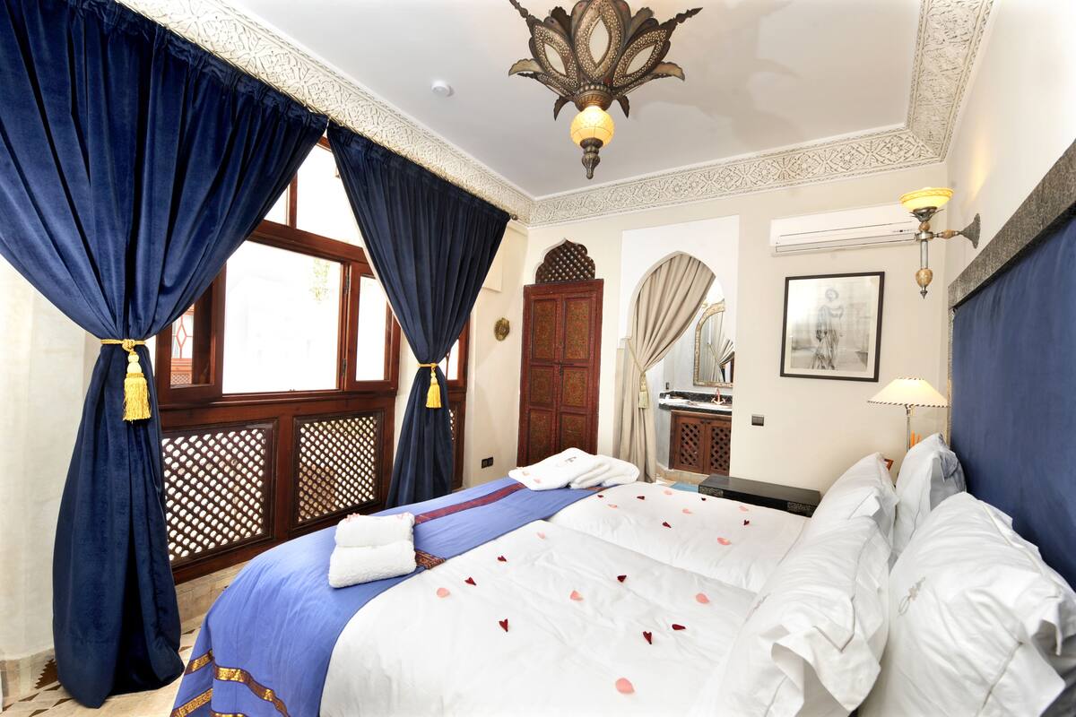 Una habitación de hotel con una cama grande, cortinas azules, una araña y una puerta de madera.