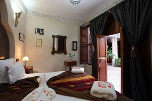 Habitación de hotel con una cama, una mesita de noche, una lámpara, un espejo y vistas al exterior.