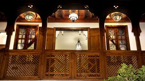 A wooden balcony with ornate lattice panels, a central light fixture, and decorative glass windows. - Riad Belle Époque (Marrakech)