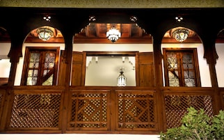 Un balcone in legno con pannelli a reticolo elaborati, un lampadario centrale e finestre con vetri decorativi.