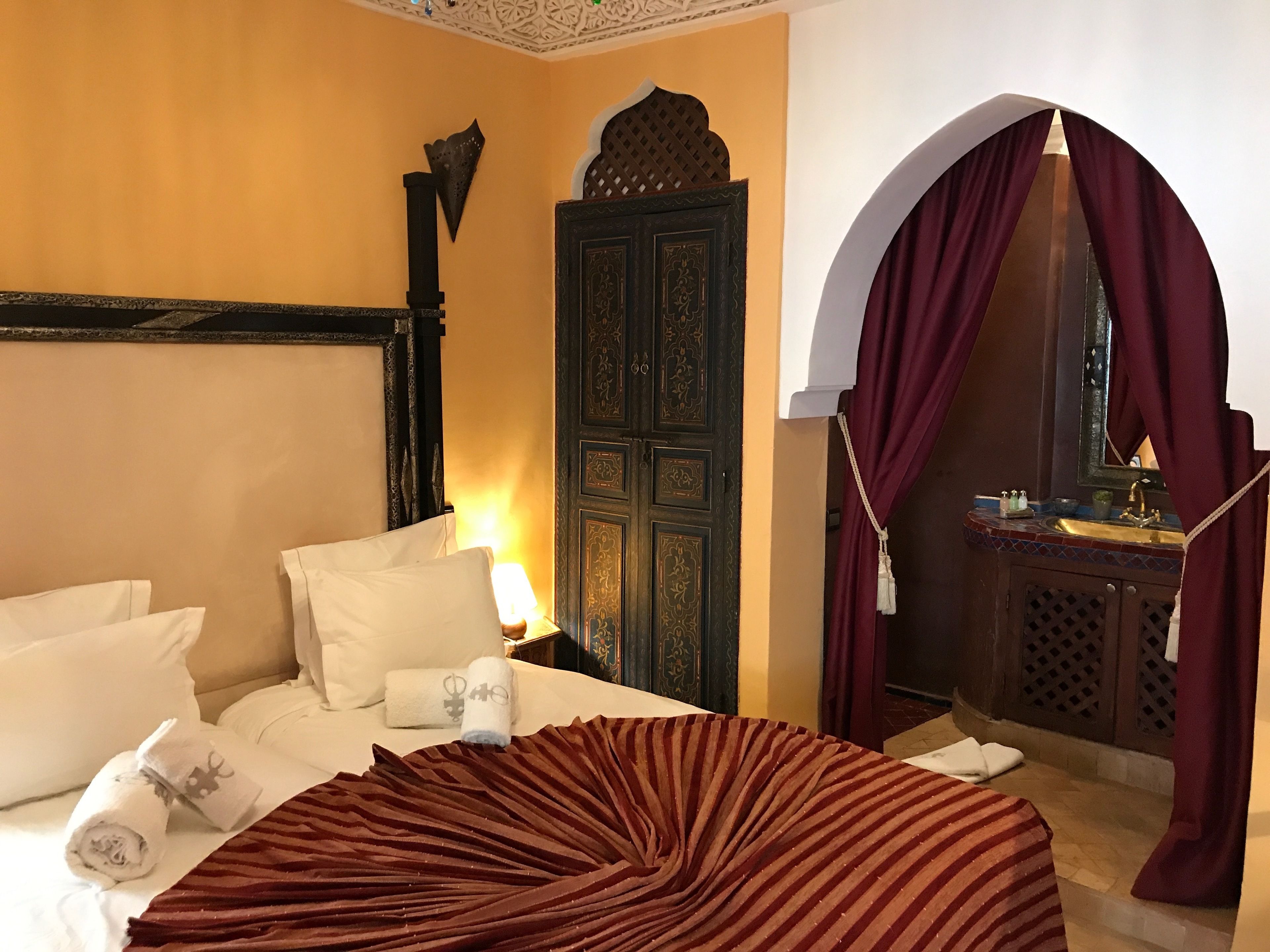 A hotel room with a bed, a nightstand, a decorative door, and a bathroom visible through an archway.