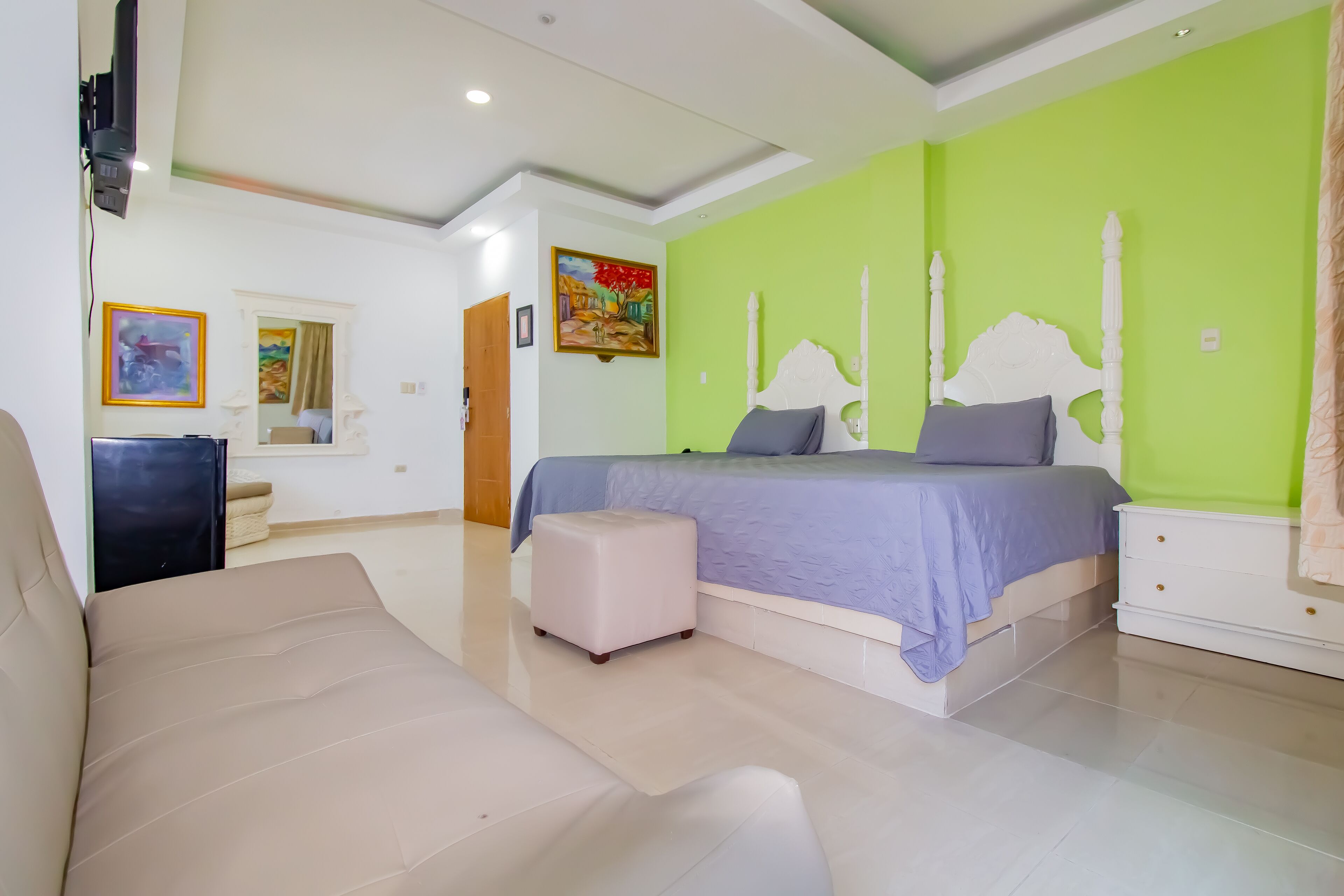 Un dormitorio con cama, sofá, un pequeño reposapiés y cómoda.