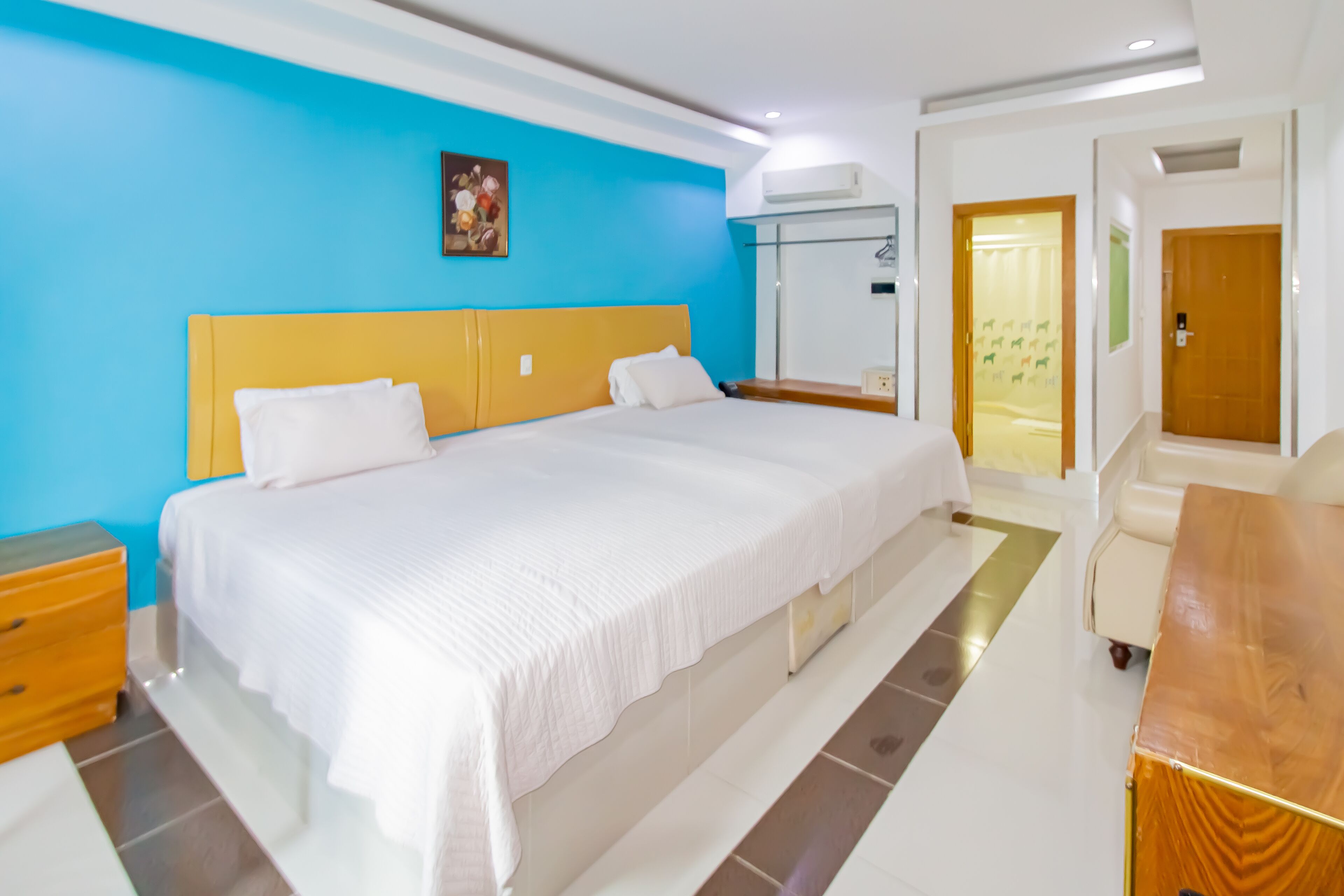 A hotel room with a large bed, a wooden nightstand, a desk, and a wardrobe.
