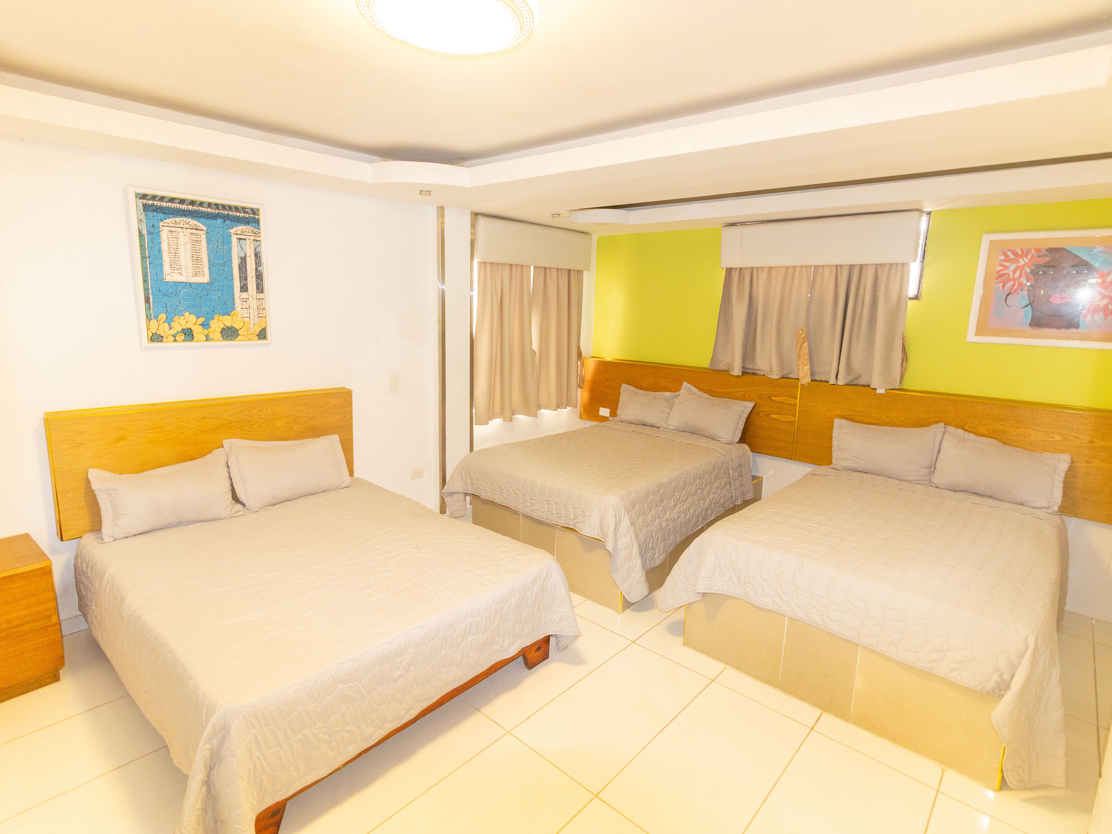 A hotel room with two beds, a wooden headboard, a window with curtains, and a painting on the wall.