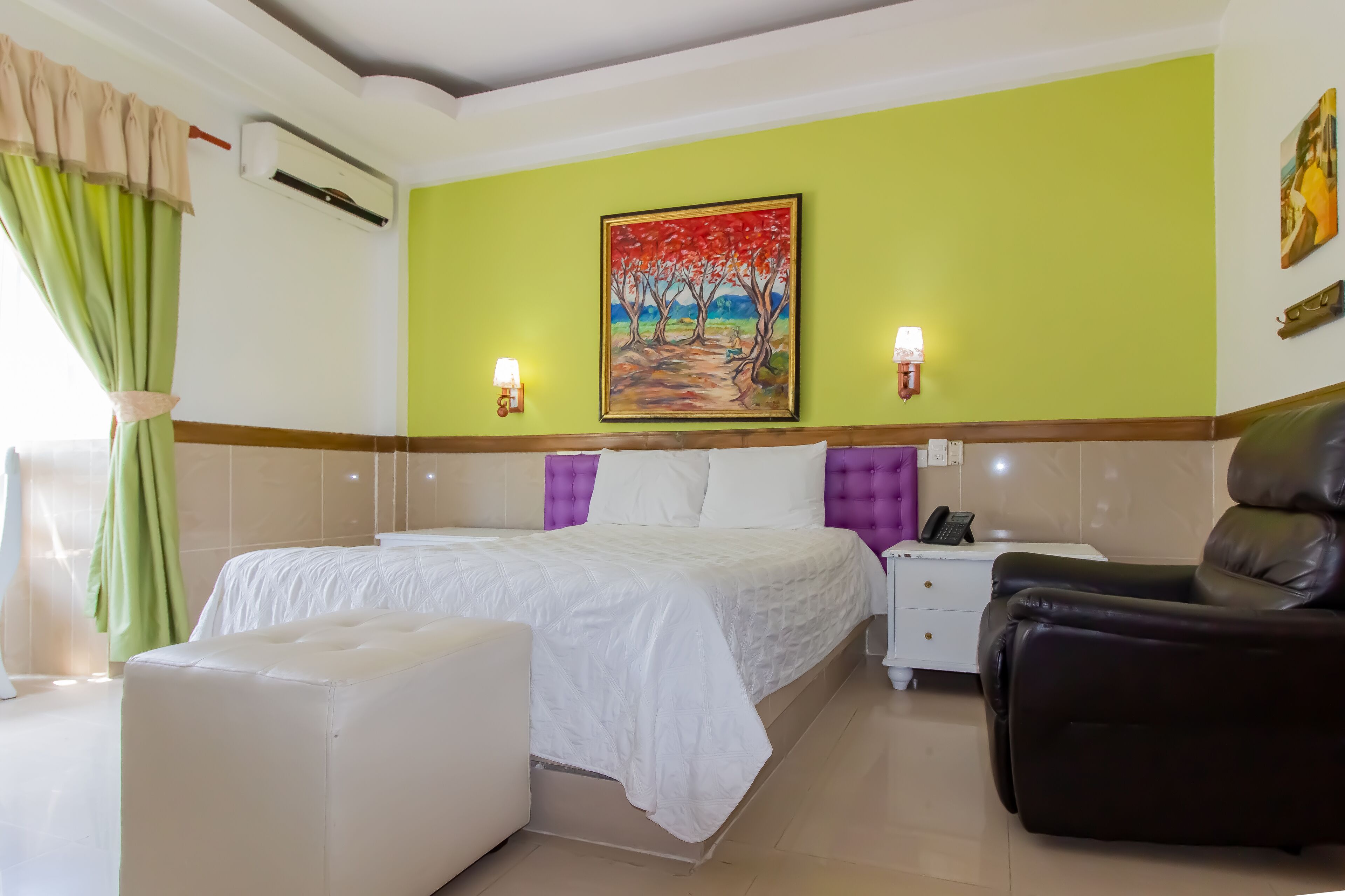 A hotel room with a bed, a massage chair, a nightstand, and a painting on the wall.