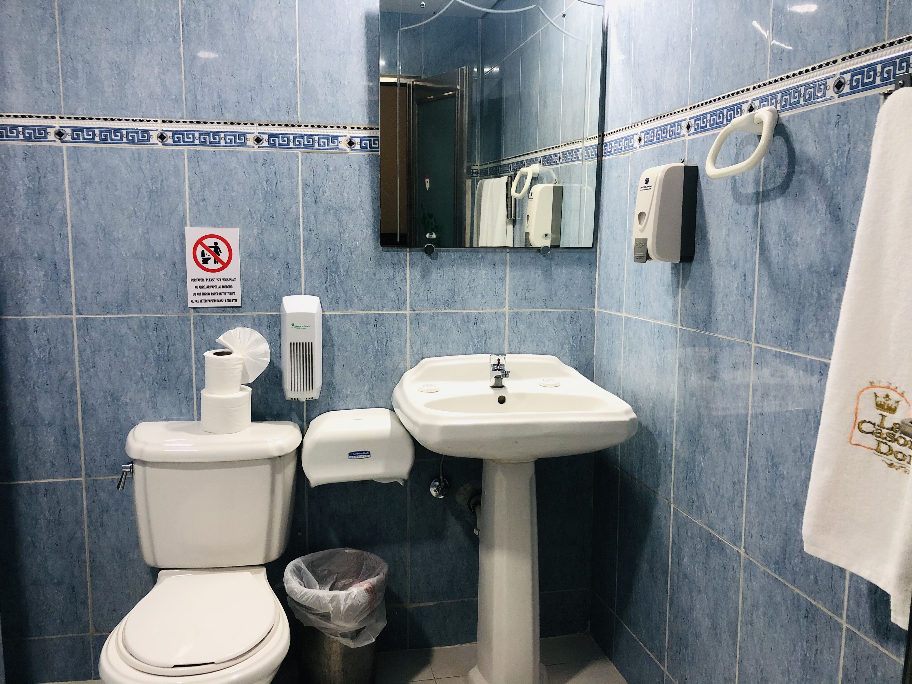 Une salle de bain équipée de toilettes, d’un lavabo, d’un sèche-mains et d’une poubelle.