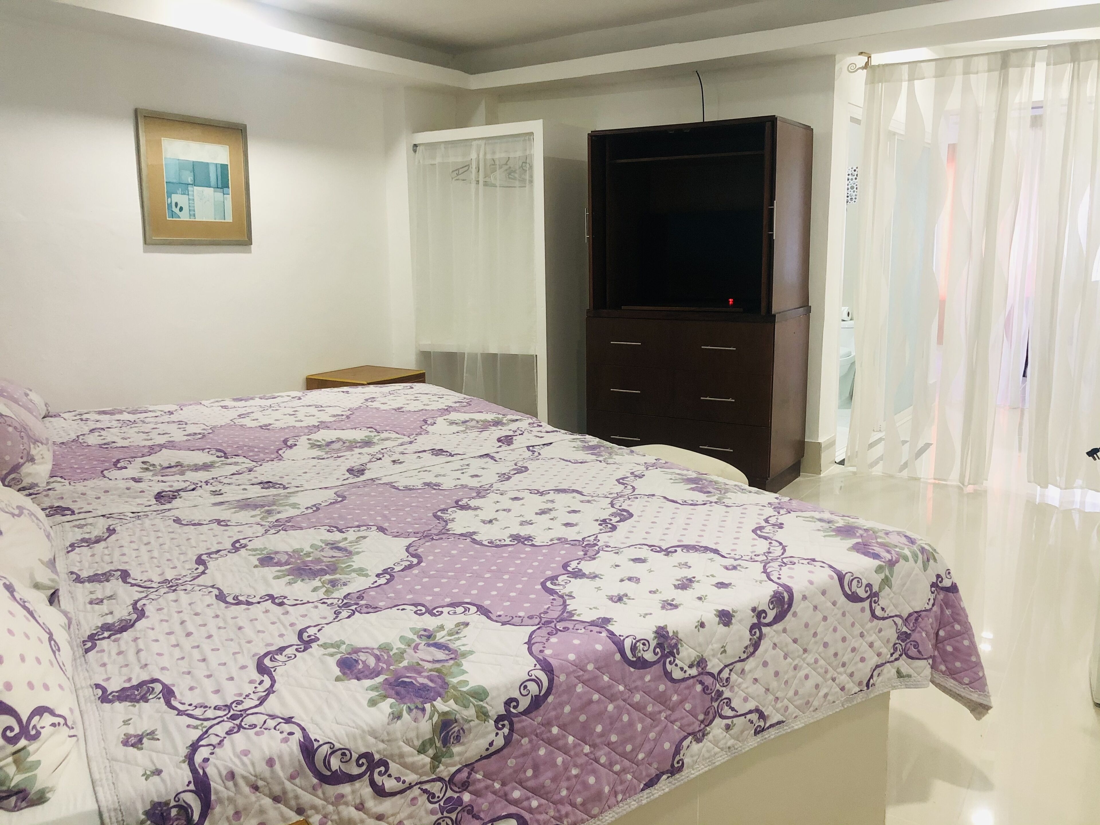 Une chambre à coucher avec un grand lit, une armoire, une télévision et une fenêtre avec des rideaux.