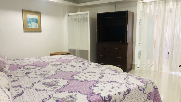 A bedroom with a large bed, a wardrobe, a television, and a window with curtains. - La Casona Dorada (Santo Domingo)