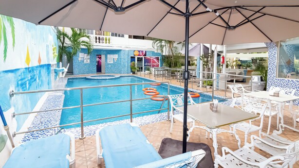 Uma área de piscina com espreguiçadeiras, uma mesa e guarda-sóis.