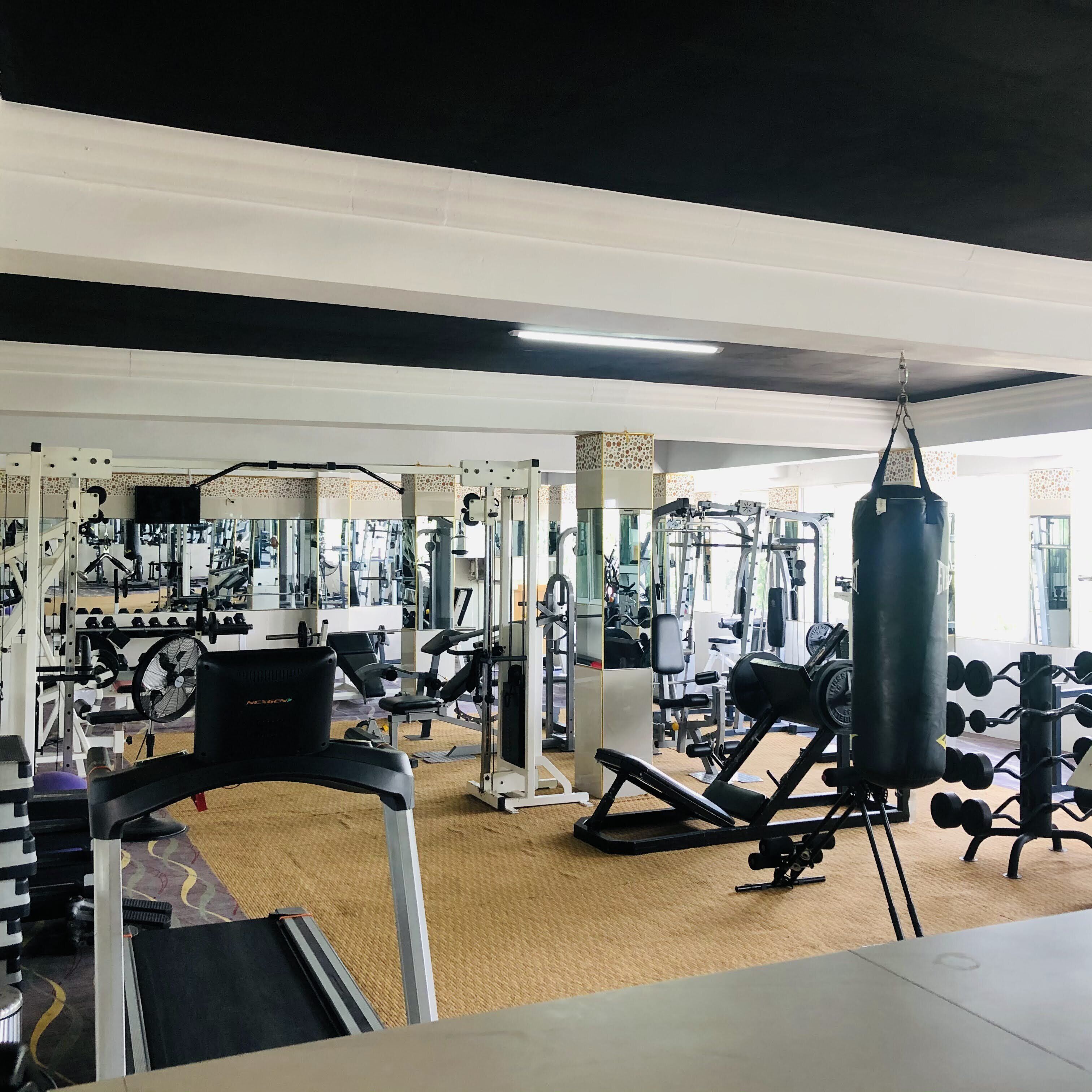 Uma academia com diversos equipamentos de exercício, incluindo esteiras, aparelhos de musculação e um saco de pancadas.