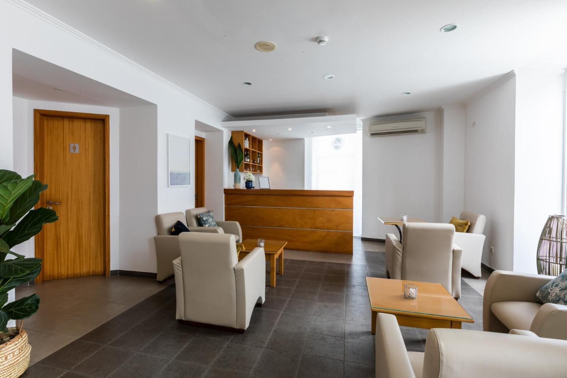 A modern hotel lobby with a reception desk, seating area, and a large plant.
