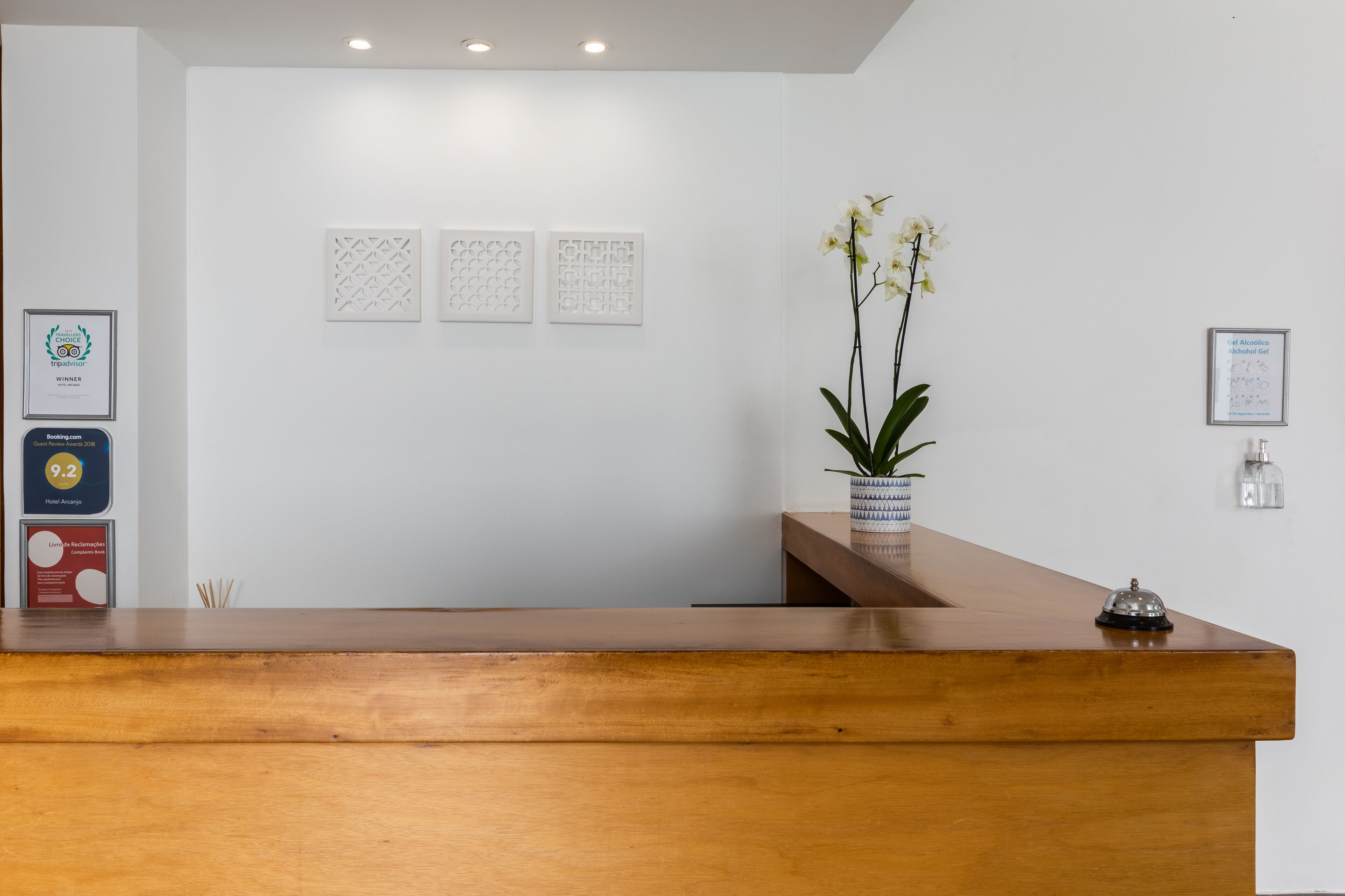 Un mostrador de recepción con detalles de madera, una orquídea en maceta y tres diplomas enmarcados en la pared.