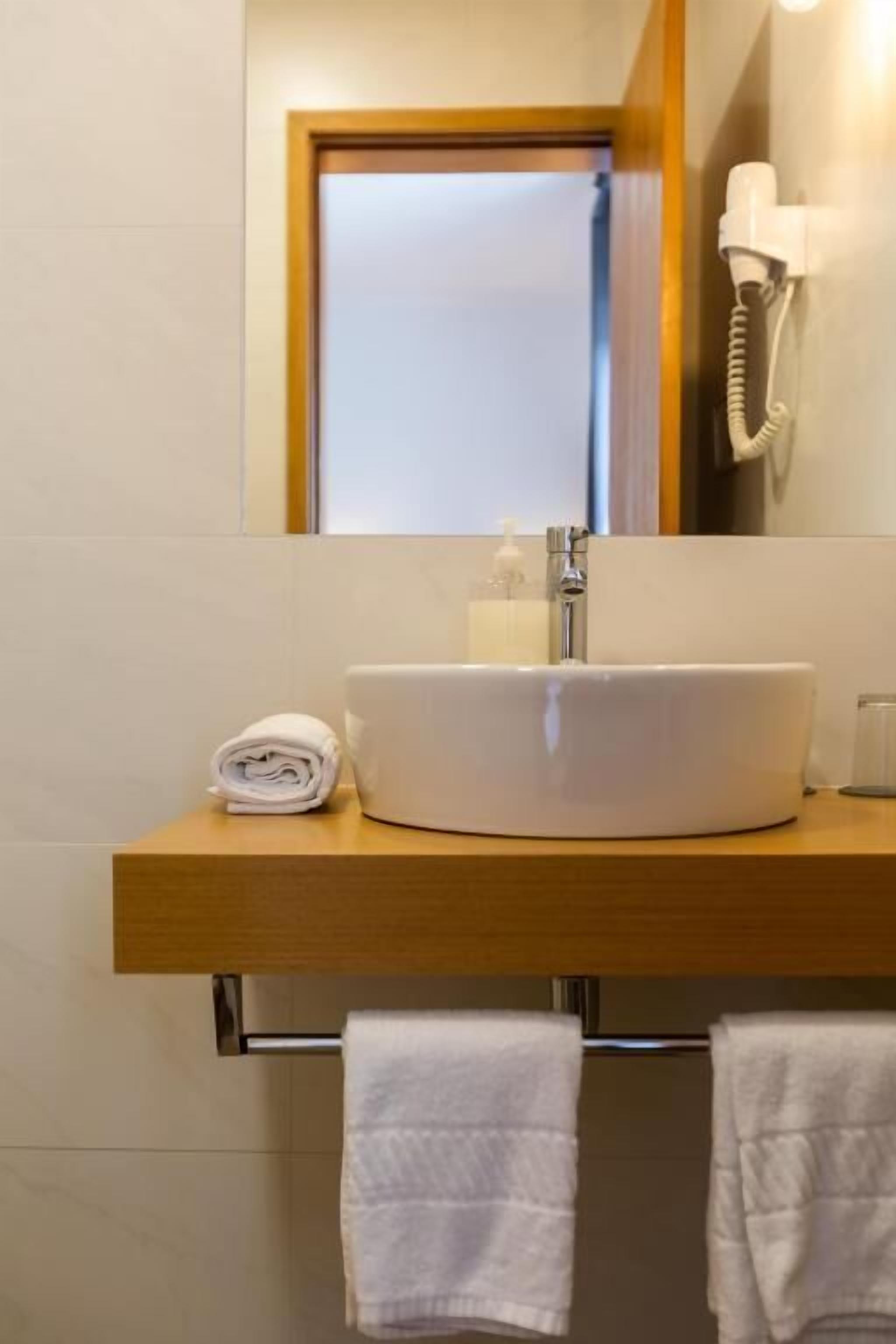 Une salle de bain avec un lavabo rond blanc, un distributeur de serviettes et un sèche-cheveux fixé au mur.