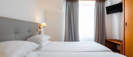 Une chambre d’hôtel avec deux lits, un téléviseur fixé au mur et un banc en bois.