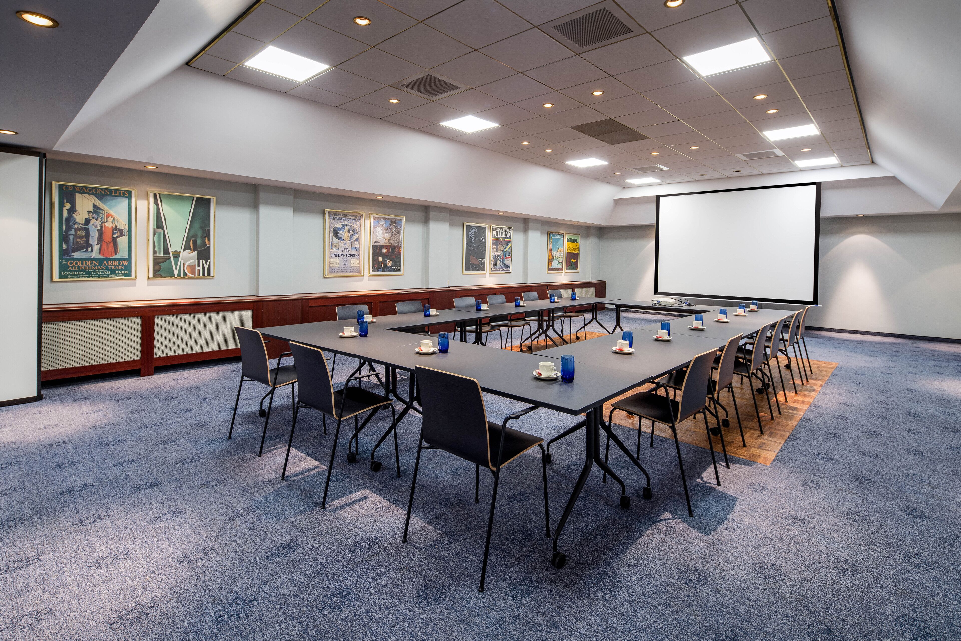Ett konferensrum med ett långt bord, stolar, en projektorduk och konstverk på väggarna.