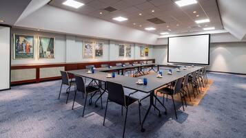 Ett konferensrum med ett långt bord, stolar, en projektorduk och konstverk på väggarna.