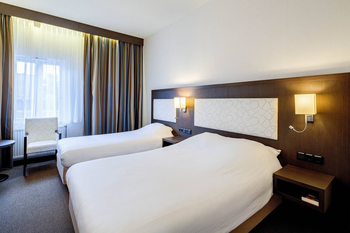 A hotel room with two beds, a chair, a nightstand, and a lamp.