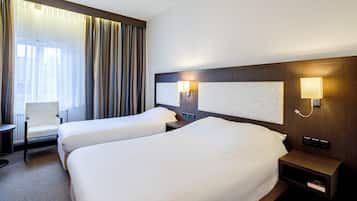 A hotel room with two beds, a chair, a nightstand, and a lamp.