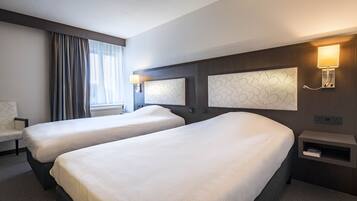 Una habitación de hotel con dos camas, una silla, una lámpara y una estantería de pared.