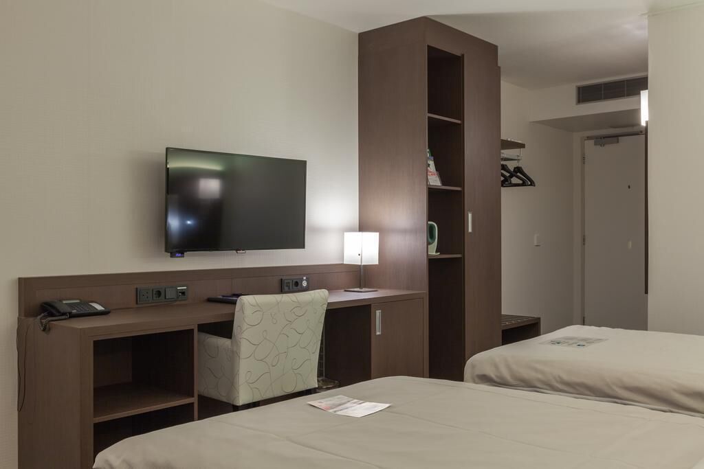 Ein Hotelzimmer mit Bett, Schreibtisch, Stuhl, Fernseher und Kleiderschrank.