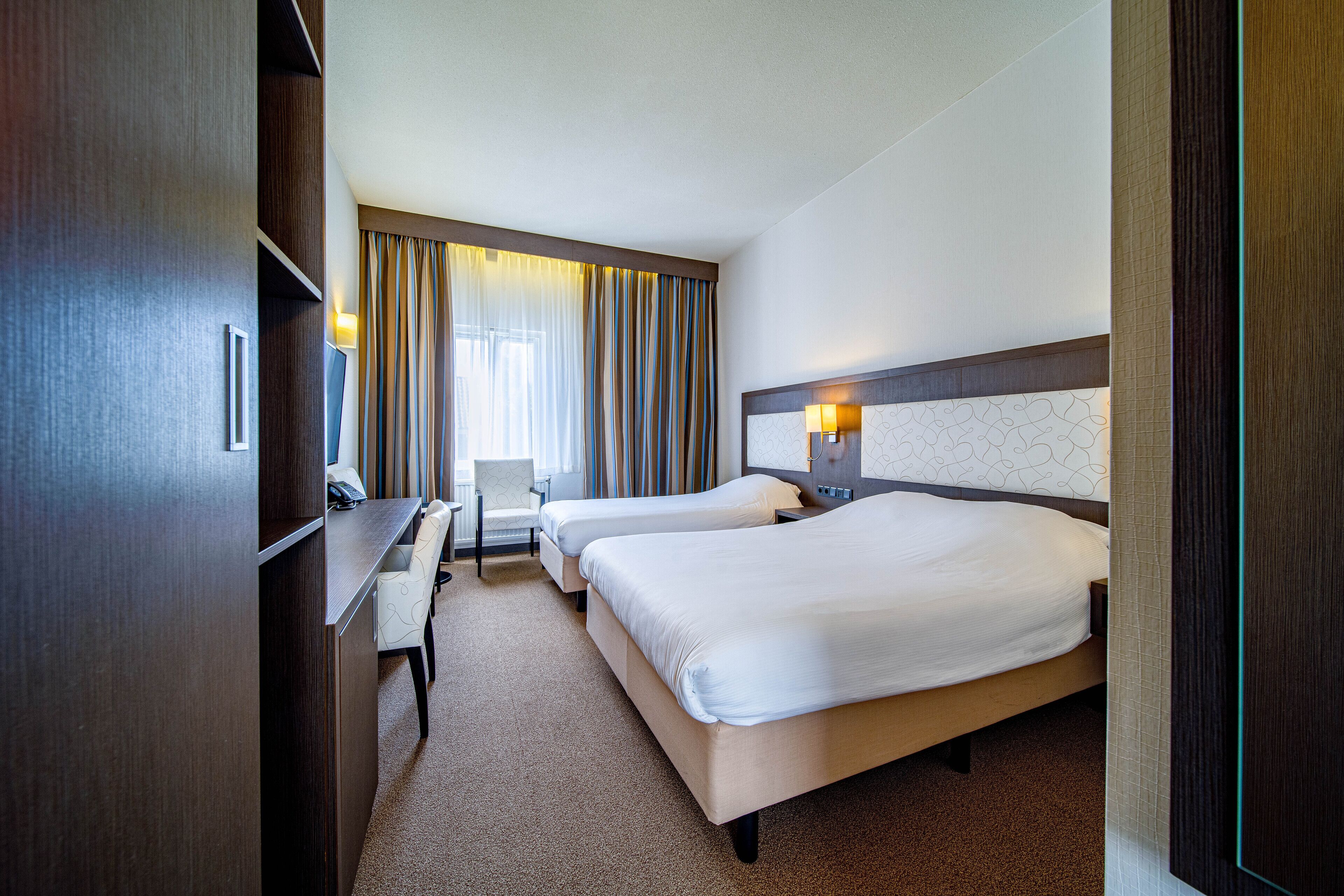 A hotel room with two beds, a desk, and a chair.