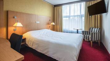 A hotel room with a large bed, two bedside lamps, a TV mounted on the wall, a desk, and a striped chair.