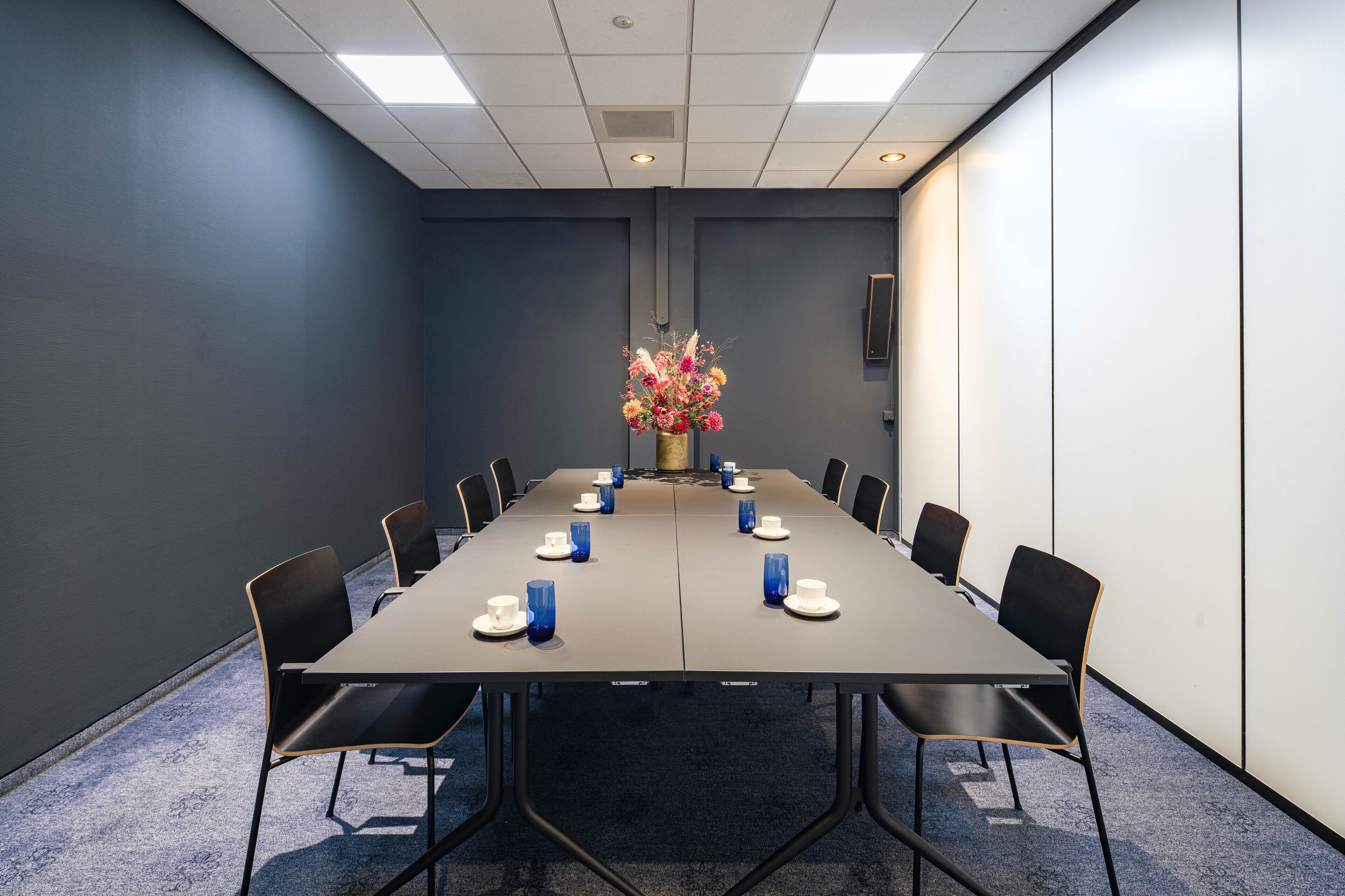 A conference room with a long table, chairs, and a floral centerpiece.