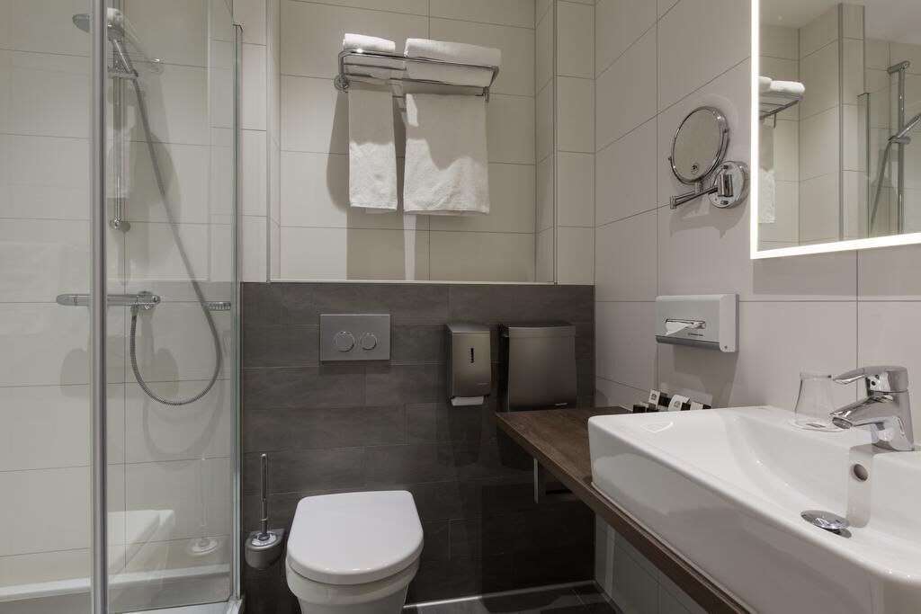 Et moderne badeværelse med brusekabine i glas, toilet, håndvask med spejl og håndklædeholdere.