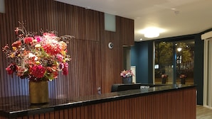 A reception desk with a wooden panel design, a vase of flowers, and a view of the outside through a window.
