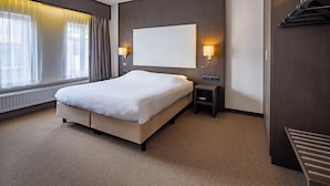 A modern hotel room with a large bed, bedside tables, a wall-mounted TV, and a view of the city through large windows.