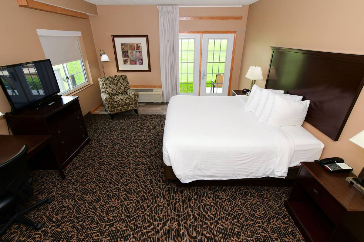 A hotel room with a large bed, a desk with a television, a chair, and a window with a view of a green lawn.