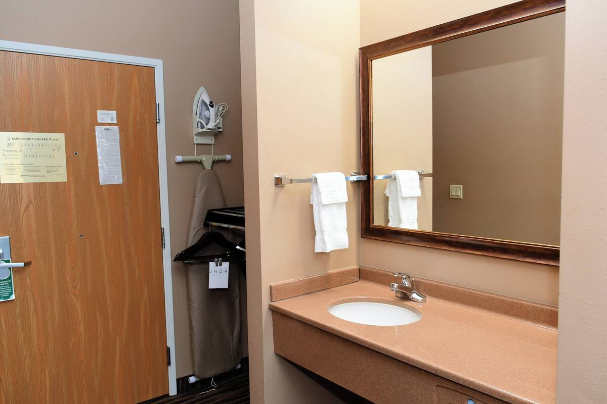 A hotel bathroom with a wooden door, a sink, a mirror, and a towel rack.