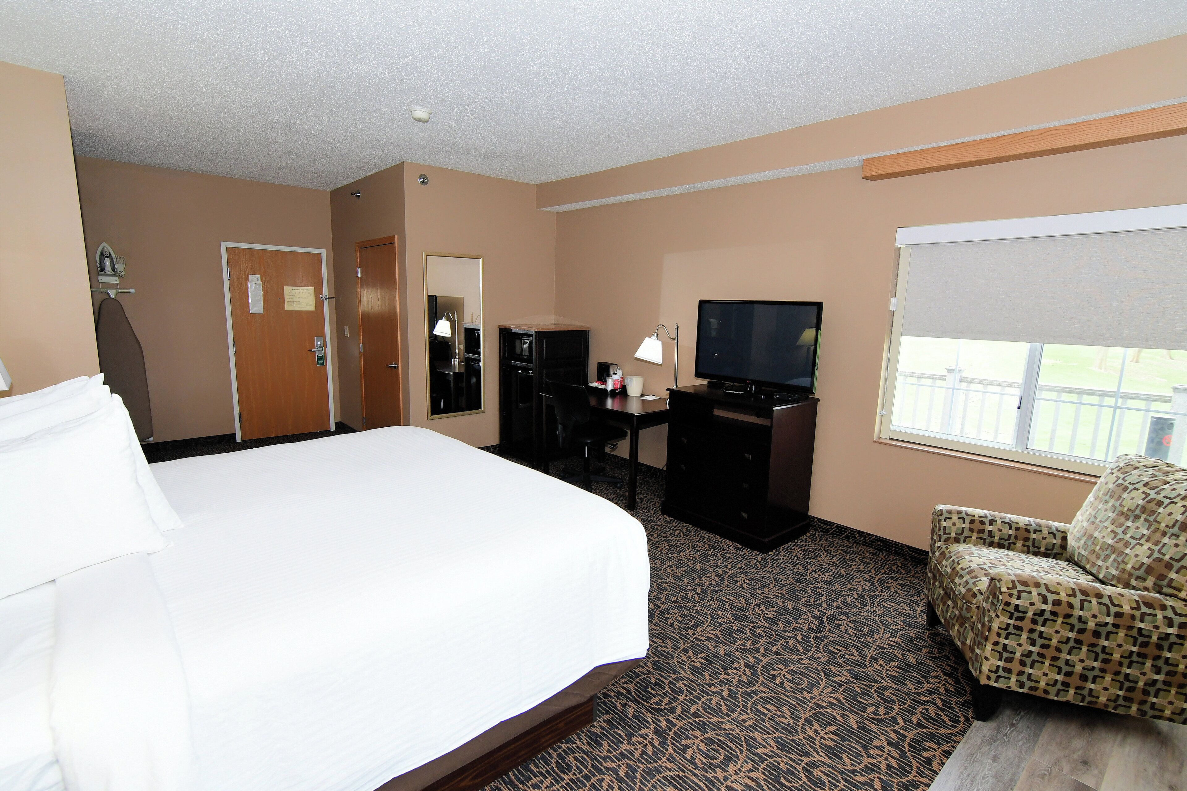 Quarto de hotel com uma cama grande, uma escrivaninha com computador, televisão e uma cadeira.
