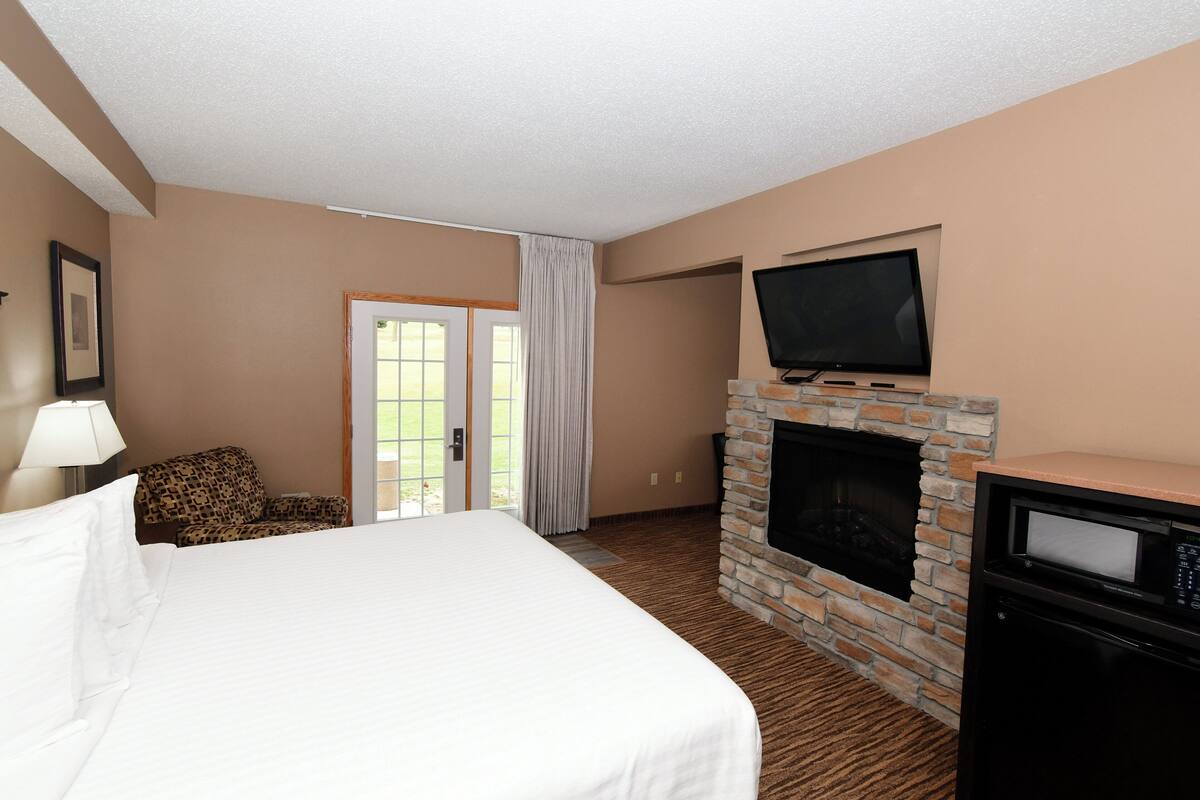 A hotel room with a large bed, a fireplace, a television, and a door leading to a balcony.