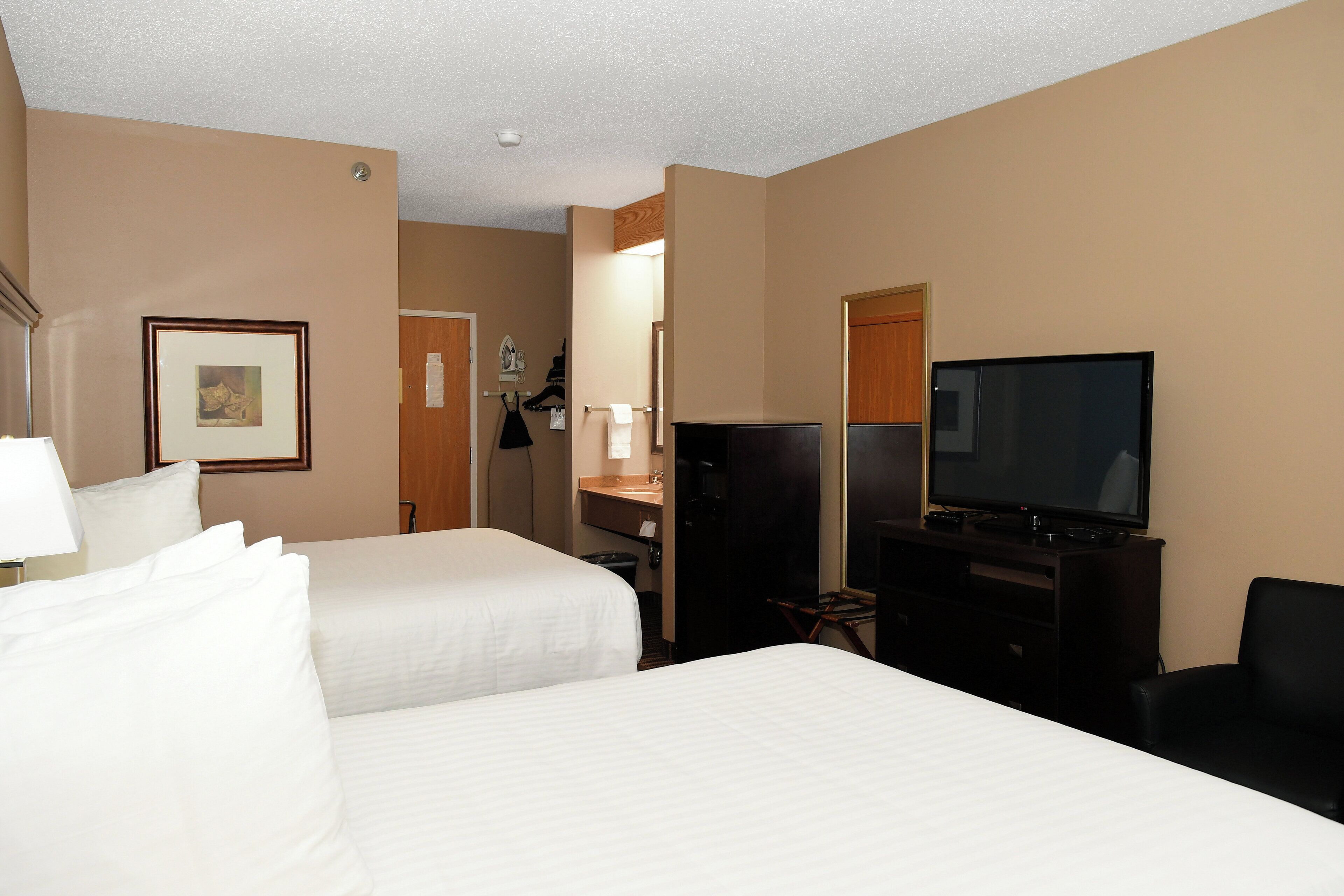 A hotel room with two beds, a TV, a desk, and a chair.