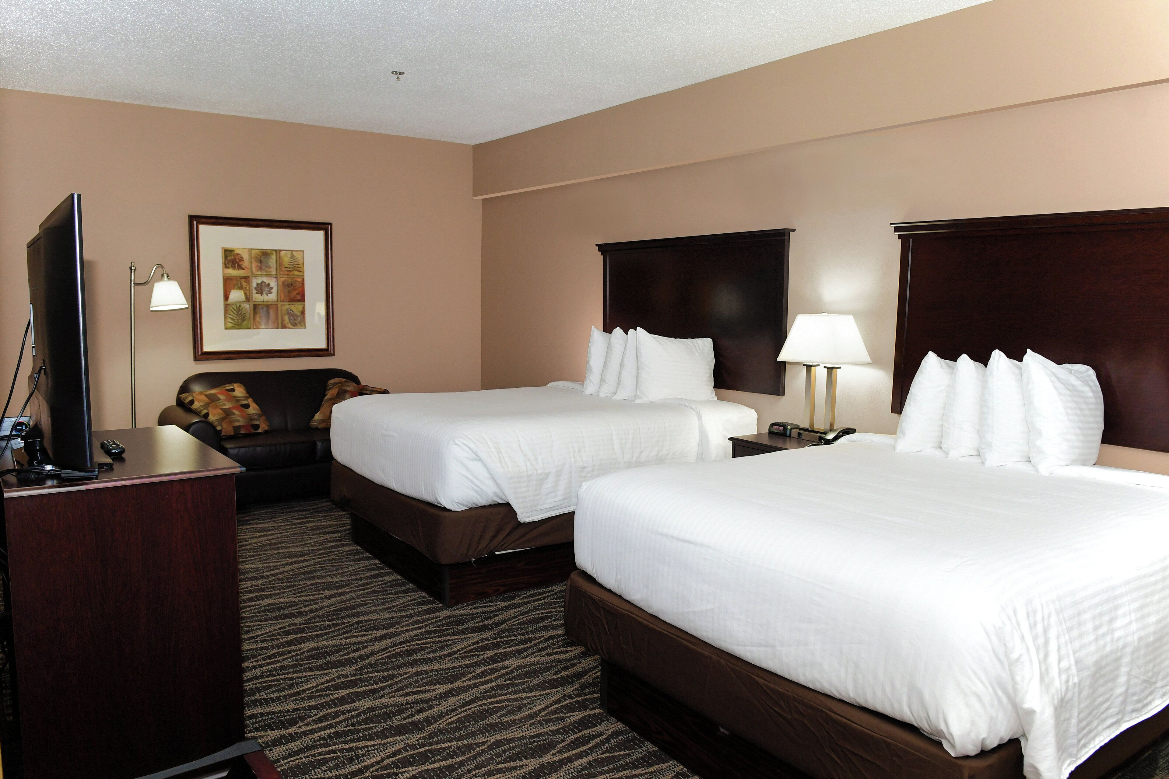A hotel room with two beds, a desk, a TV, and a framed picture on the wall.