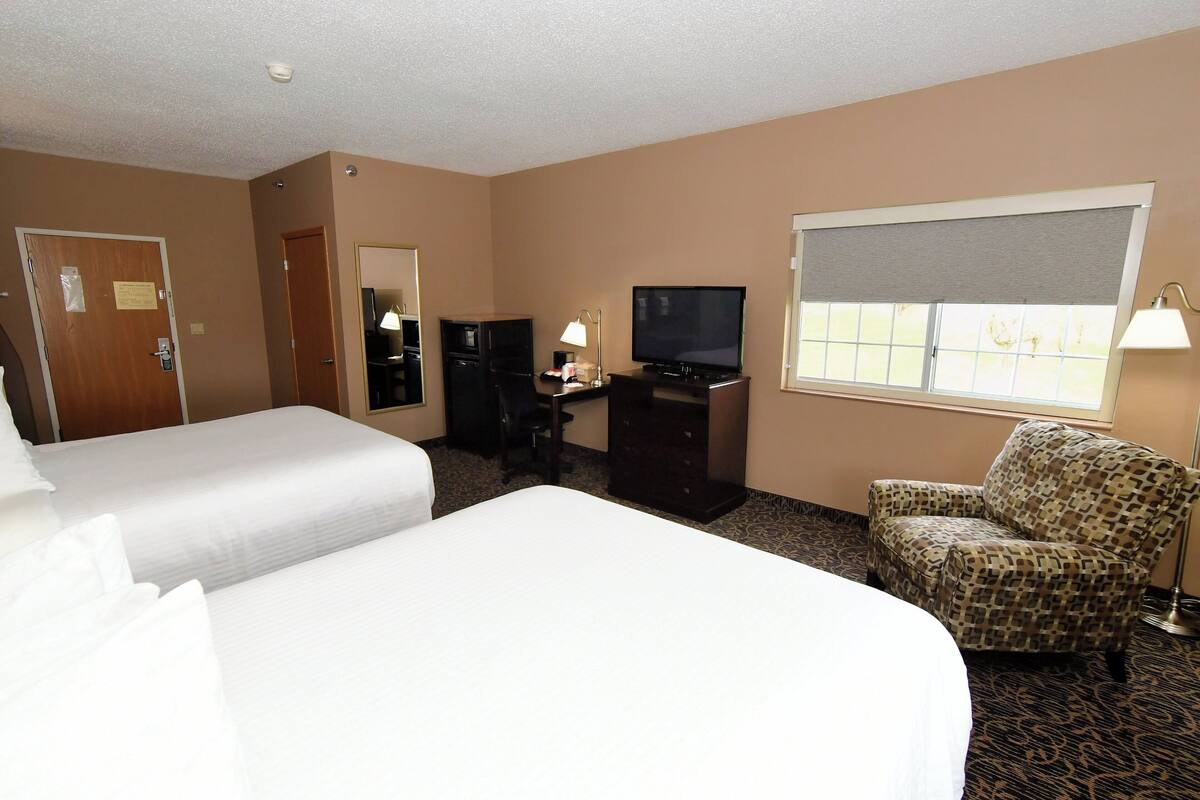 A hotel room with two beds, a desk with a TV, a chair, and a window with a view.