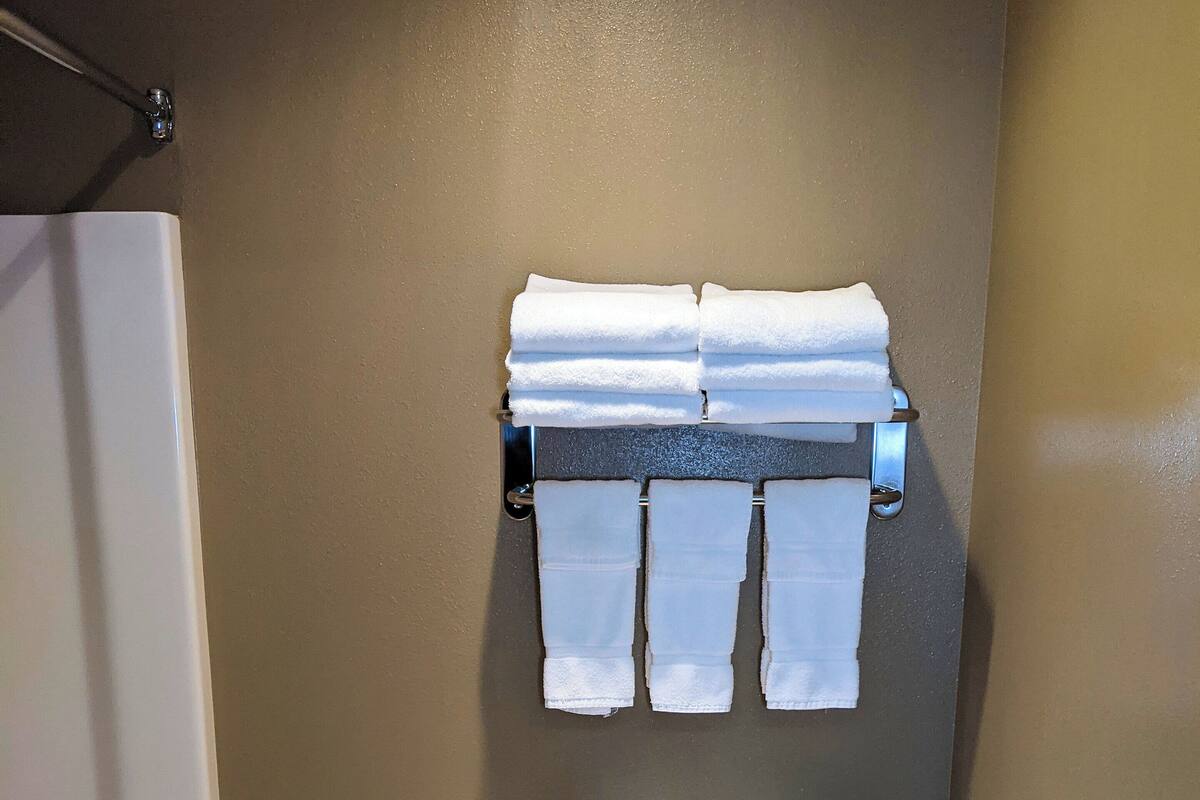 A bathroom with a toilet, a towel rack with multiple towels, a trash bin, and a bathtub.