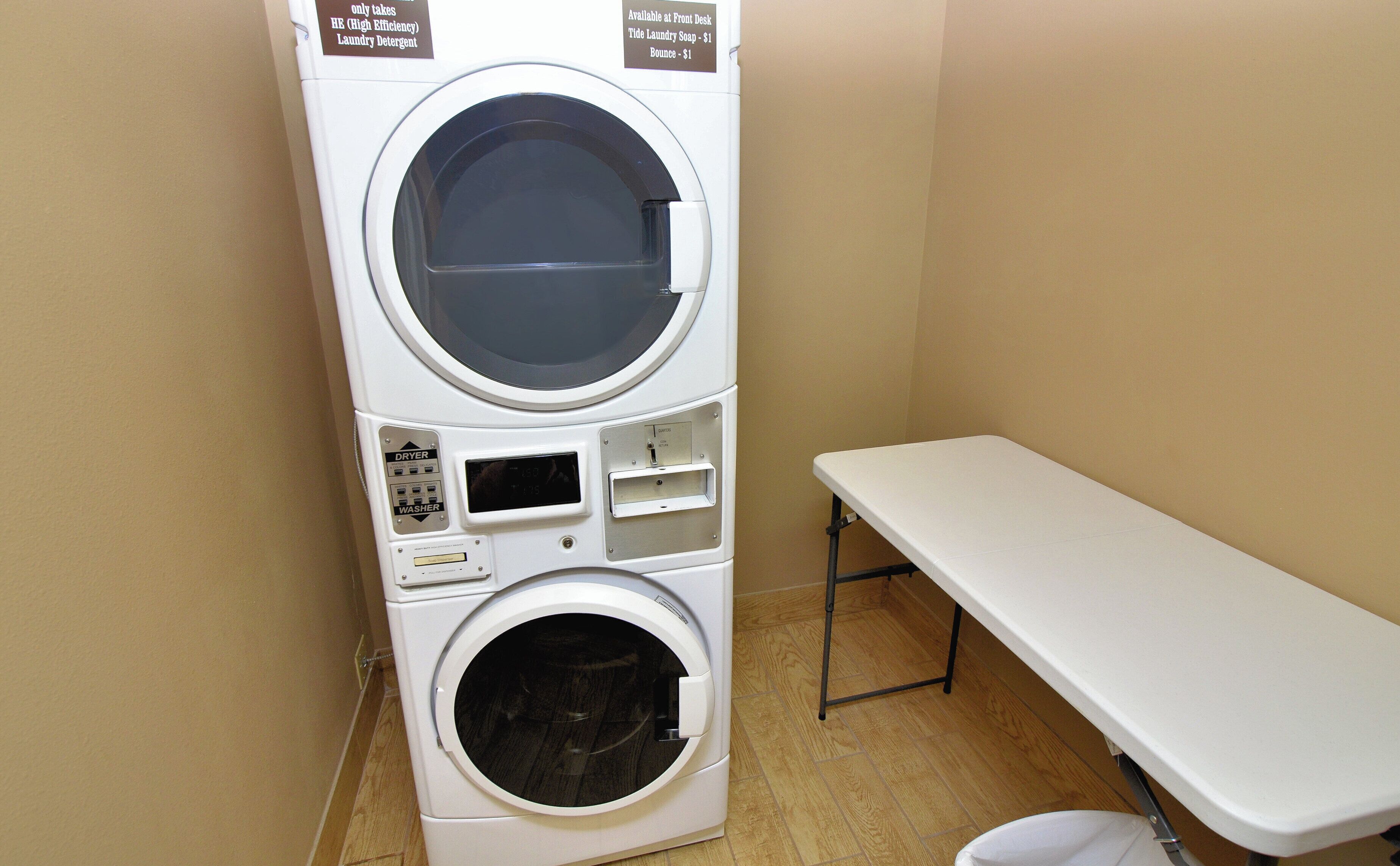 A stacked washer and dryer unit with a table beside it.