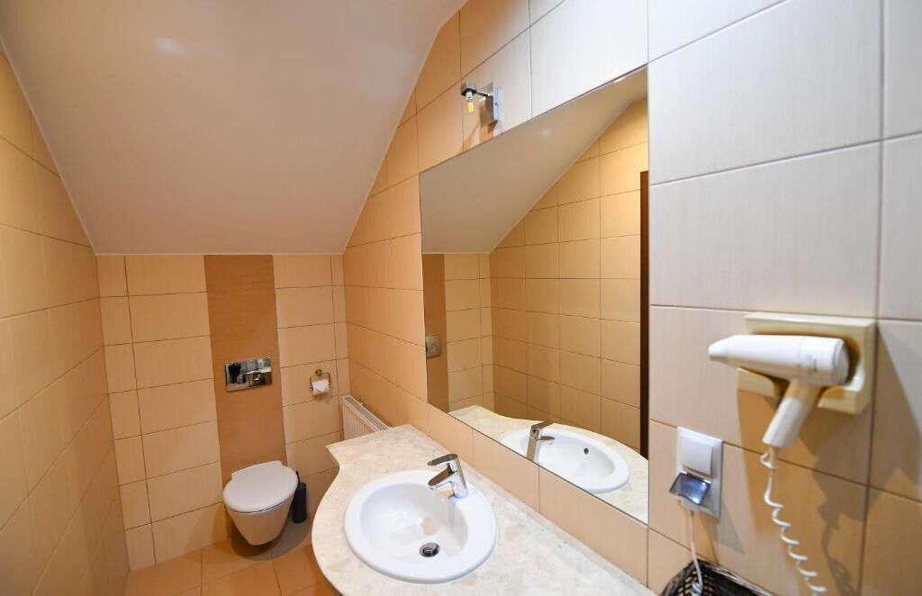 Un baño con inodoro, dos lavamanos, un espejo y un secador de pelo en la pared.