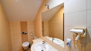 Un baño con inodoro, dos lavamanos, un espejo y un secador de pelo en la pared.