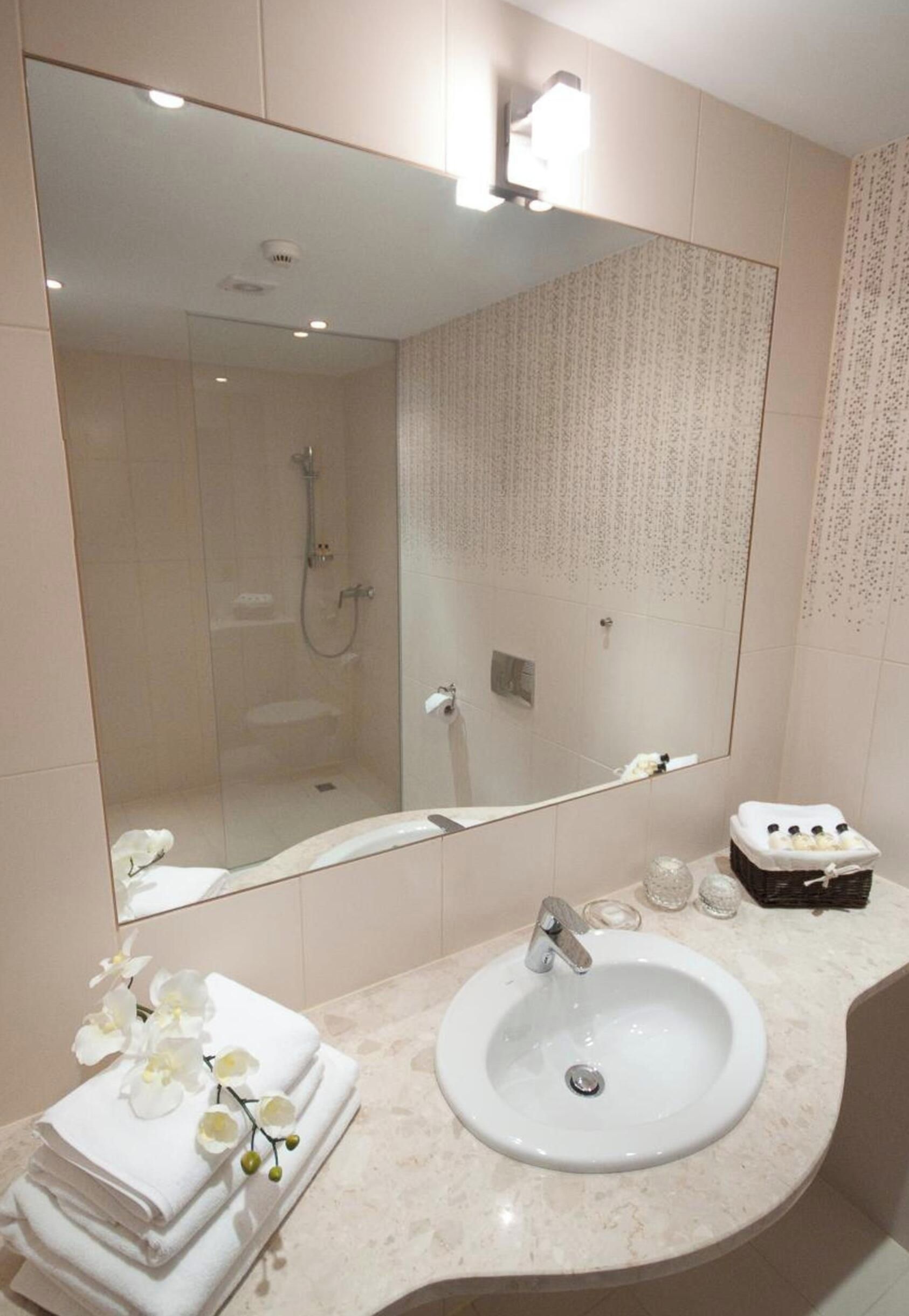 Ein Badezimmer mit einem großen Spiegel, einem Waschbecken und einer Dusche.