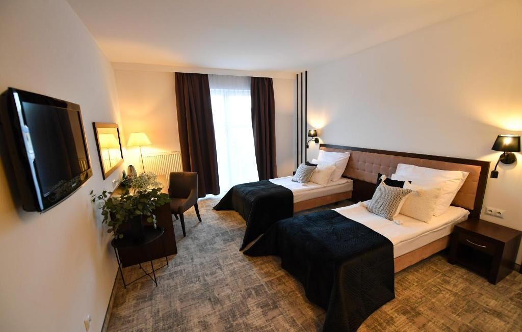 A hotel room with two beds, a television, a desk with a chair, and a potted plant.
