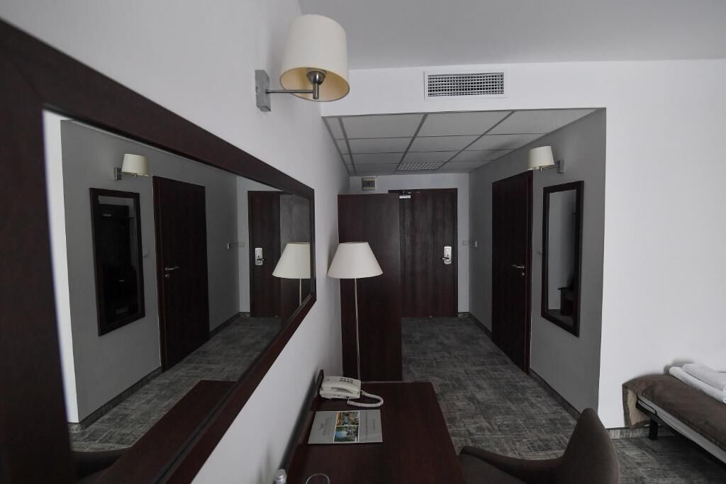 A hotel room with a desk, chair, two bedside lamps, a telephone, and a mirror.