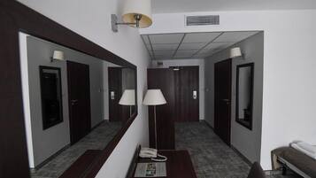 A hotel room with a desk, chair, two bedside lamps, a telephone, and a mirror.