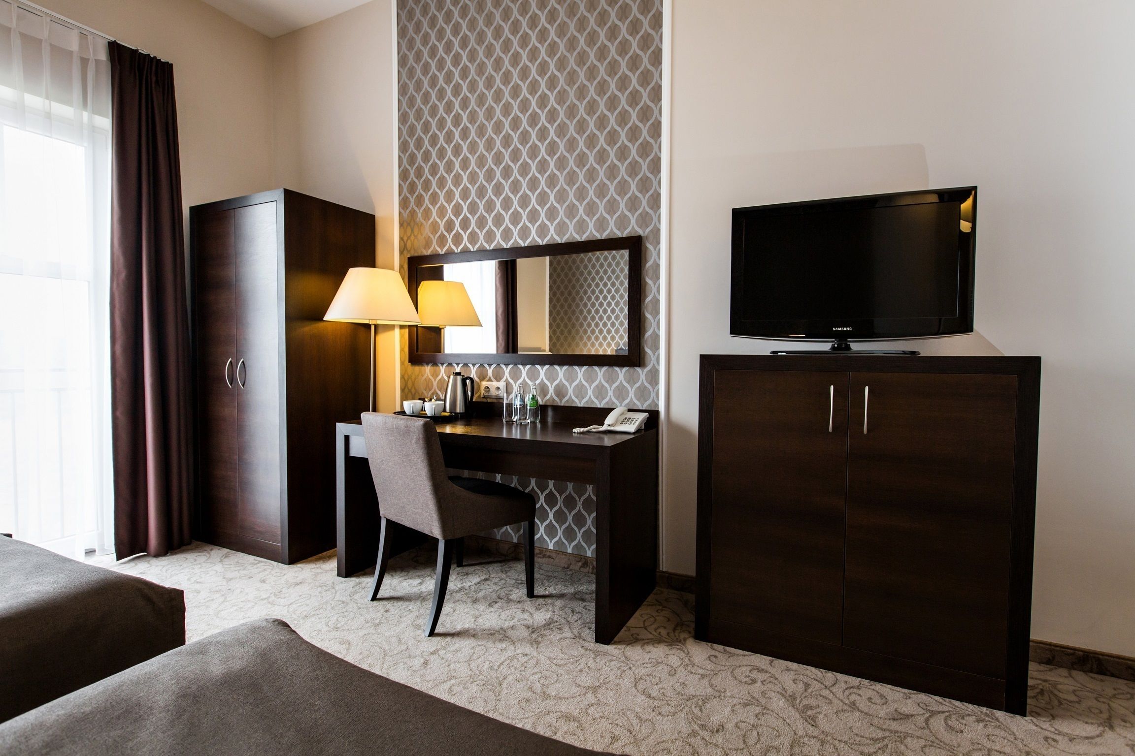 Habitación de hotel con cama, escritorio con silla, televisor, armario y lámpara.