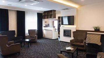 A hotel lobby with seating areas, a bar, a flat-screen TV, and a fireplace.